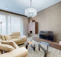 Nappali egy háromszobás lakásban bézs kanapéval, mintás fallal és üvegasztallal.