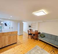 Egyszobás lakás nappali része kanapéval, étkezőasztal, konyha és fa dekorációjú padló.