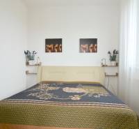 Hálószoba egy kétszobás lakásban világos ággyal és dekoratív képekkel a falon.