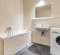 Fürdőszoba káddal, mosdóval és mosógéppel egy háromszobás lakásban. A falak bézs csempével borítva.