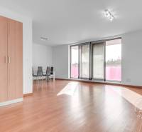 Világos nappali egy háromszobás lakásban, fa mintázatú padlóval és erkéllyel.