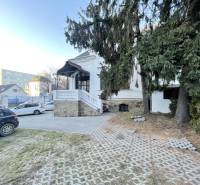 Az épület a Vajanského utcában, Eperjesen, a bevezető úttal, autókkal és fenyőfákkal az előtérben.