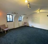 Az épület belső tere íves ablakokkal, zöld szőnyeggel és fali táblával.