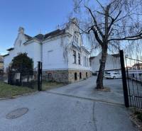 Épület a Vajanského utcában, Eperjesen, fával és parkoló autókkal.