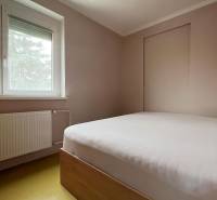 Hálószoba családi házban, egyszerű ággyal, ablakkal és radiátorral.