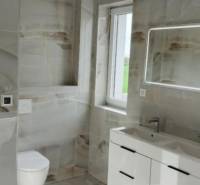 Fürdőszoba modern mosdóval, világítással ellátott tükörrel és csempékkel egy háromszobás lakásban.