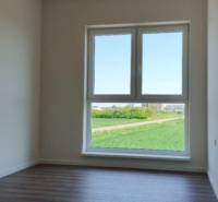 Világos szoba egy háromszobás lakásban fa mintázatú padlóval és nagy ablakkal.