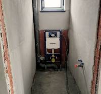 WC építési előkészítése családi házban beépített tartállyal, fehér falakkal és kis ablakkal.