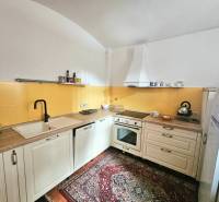 Konyha egy háromszobás lakásban krémszínű szekrényekkel, sárga csempével és mintás szőnyeggel.