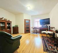 Nappali egy háromszobás lakásban, fa dekorációjú padlóval, kanapéval és televízióval felszerelve.