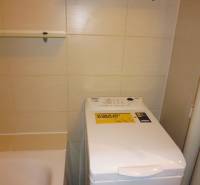 Fürdőszoba egy kétszobás lakásban, mosógéppel a kád mellett és polcokkal.