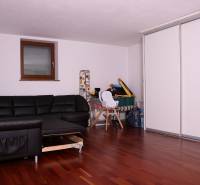 Családi ház fekete kanapéval, fehér szekrényekkel és fa mintázatú padlóval.