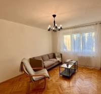 Nappali kanapéval, fotellel, csillárral és fa dekorációjú padlóval egy háromszobás lakásban.