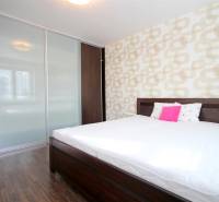 Hálószoba egy kétszobás lakásban ággyal, beépített szekrénnyel és fa dekoros padlóval.