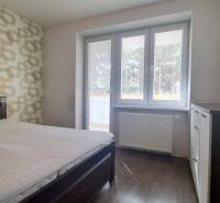 Hálószoba egy kétszobás lakásban ággyal, mintás tapétával és fa dekorációjú padlóval.