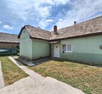 Családi ház Ajnácskőn aszfaltos járdával és zöld gyepes udvarral a kék ég alatt.