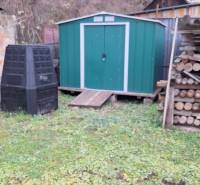 Családi ház Ajnácskőn zöld kerti házzal, komposztálóval és fatárolóval.