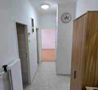 Előszoba egy 3 szobás lakásban, csempével, fehér falakkal és fa dekorációval a bútorokon.