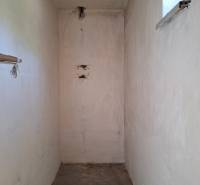 Szűk belső tér egy családi házban kis ablakkal és betonpadlóval.