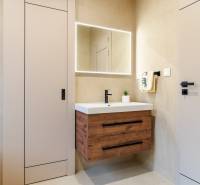 Fürdőszoba egy háromszobás lakásban, megvilágított tükörrel és fa dekorációjú szekrénnyel.