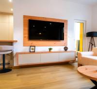 Nappali egy háromszobás lakásban, fa dekoros padlóval, televízióval és krémszínű kanapékkal.