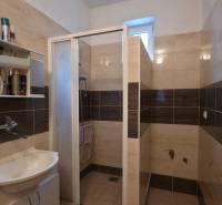 Fürdőszoba mosdóval és zuhanyzóval, világos tónusú csempékkel.