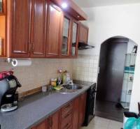 Konyha egy háromszobás lakásban, fa szekrényekkel és csempézett fallal a munkalap felett.