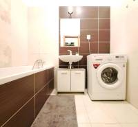 Fürdőszoba egy kétszobás lakásban mosógéppel, káddal és mosdóval.