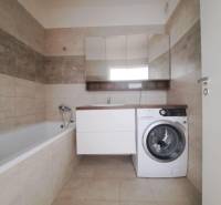 Fürdőszoba egy kétszobás lakásban káddal, mosógéppel és bézs csempékkel.