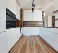 Konyha egy kétszobás lakásban fehér szekrényekkel és fa dekor padlóval.