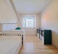 Családi ház szobája ággyal, könyvespolccal és fa dekorációjú padlóval.