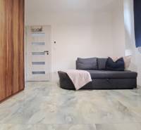 Egy családi ház szobája kanapéval, szekrénnyel, ajtóval és márvány mintás padlóval.