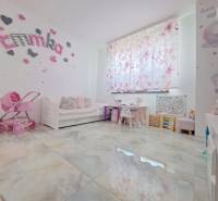 Gyerekszoba egy családi házban dekorációkkal, babakocsival és íróasztalokkal. A padló fa mintázatú.