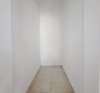 Keskeny folyosó egy családi házban fehér falakkal és világos padlóval.