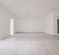 Tágas szoba fa mintázatú padlóval és fehér falakkal egy családi házban.