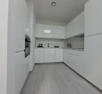 Modern konyha fehér szekrényekkel és fa dekor padlóval egy kétszobás lakásban.