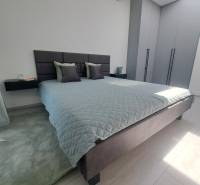 Hálószoba nagy ággyal, szürke szekrényekkel és fekete csillárral egy kétszobás lakásban.