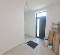 Családi ház előszobája járólappal, az ajtó mellett lépcső és anyag található.