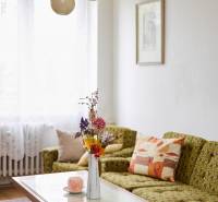 Világos nappali egy háromszobás lakásban kanapéval, asztallal és dekoratív virágokkal vázában.