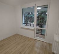 Szoba világos falakkal, fa mintázatú padlóval és kilátással a zöldre.