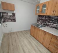 A háromszobás lakás konyhája fa dekor padlóval és egyszerű szekrényekkel rendelkezik.