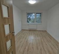 Tágas szoba egy háromszobás lakásban, fa mintás padlóval és nagy ablakkal.