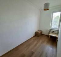 Szoba egy négy szobás lakásban egyszerű bútorokkal és fa dekorációjú padlóval.