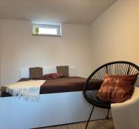 Hálószoba családi házban egyszerű ággyal és kényelmes fotellel.