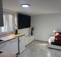 Nappali egy családi házban fehér konyhabútorral és sötétbarna kanapéval.