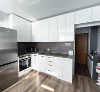 Konyha fehér szekrényekkel és fa mintázatú padlóval egy egyszobás lakásban.