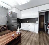 Konyha egy egyszobás lakásban, fa dekor padlóval, fehér szekrényekkel és kanapéval.