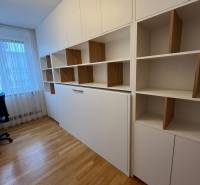 Irodai szoba háromszobás lakásban polcokkal és fa dekorációjú padlóval.