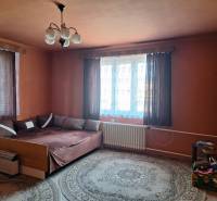 Egy szoba családi házban ággyal, szőnyeggel, függönyökkel és éjjeliszekrénnyel.