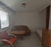 Egyszobás lakás egy székkel, asztallal és komóddal, fa dekoros padlóval.